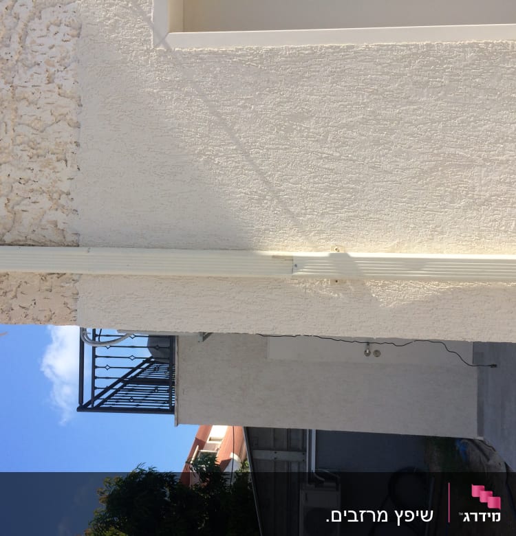 קיר חיצוני עם מרזב לבן על רקע שמיים כחולים